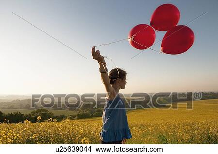Picture - Girl carrying balloons in field. Fotosearch