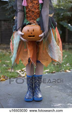Stock Image - Girl in Halloween costume with pumpkin. Fotosearch