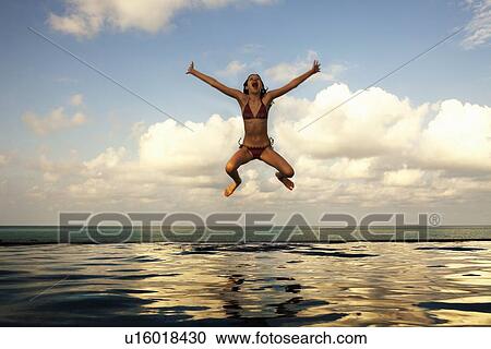 Stock Image - Girl jumping into infinity pool. Fotosearch