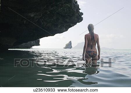 Stock Image - Girl standing in water under rocks. Fotosearch