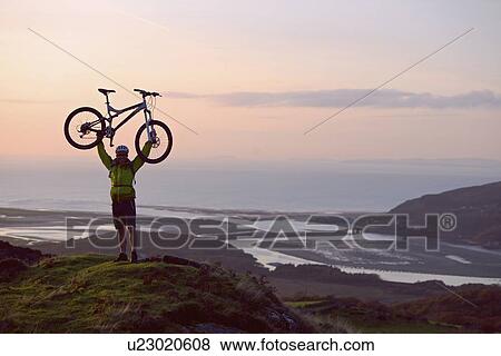 Man holding bicycle on hilltop View Large Photo Image Stock Photo - Man holding bicycle on hilltop. Fotosearch