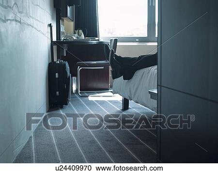 Stock Image - Man laying on hotel room bed. Fotosearch
