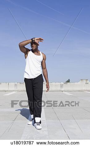 Stock Photo - Man shielding his eyes on urban rooftop. Fotosearch