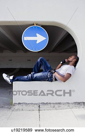 Stock Photo - Man sitting on ledge on city street. Fotosearch