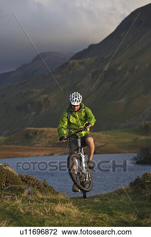 Stock Image - Mountain biker on grassy hillside. Fotosearch