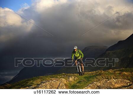 Stock Image - Mountain biker on grassy hillside. Fotosearch