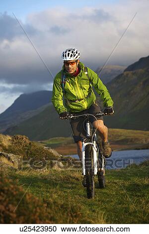 Stock Image - Mountain biker on grassy hillside. Fotosearch