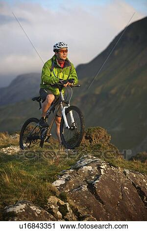 Stock Image - Mountain biker standing on hilltop. Fotosearch