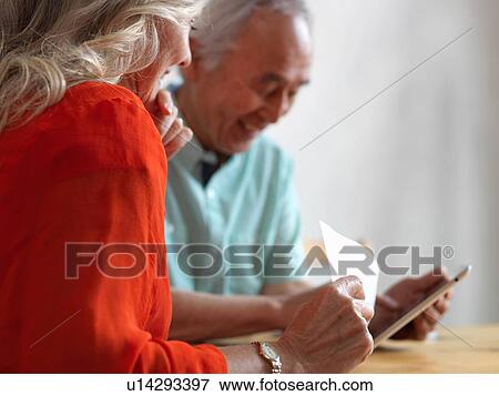Stock Photo - Older couple reading mail in kitchen. Fotosearch