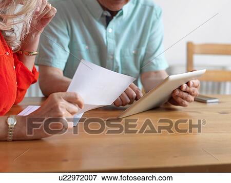 Stock Photo - Older couple reading mail in kitchen. Fotosearch