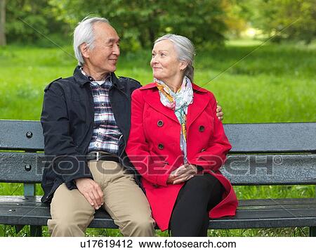 Stock Image - Older couple sitting on park bench. Fotosearch