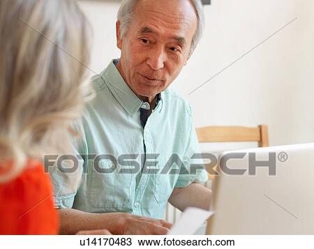 Stock Image - Older couple talking in kitchen. Fotosearch