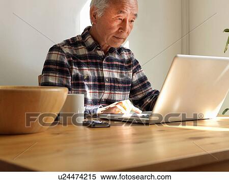 Stock Photography - Older man using laptop at table. Fotosearch