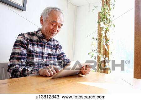 Older man using tablet computer at table View Large Photo Image Stock Image - Older man using tablet computer at table. Fotosearch