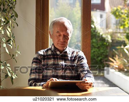 Stock Image - Older man using tablet computer at table. Fotosearch