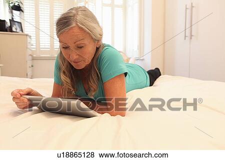 Stock Photo - Older woman using tablet computer on bed. Fotosearch