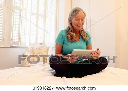 Older woman using tablet computer on bed View Large Photo Image Stock Photo - Older woman using tablet computer on bed. Fotosearch