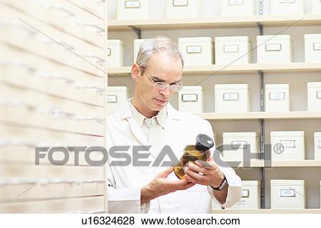 Stock Photo - Pharmacist examining bottle of syrup. Fotosearch