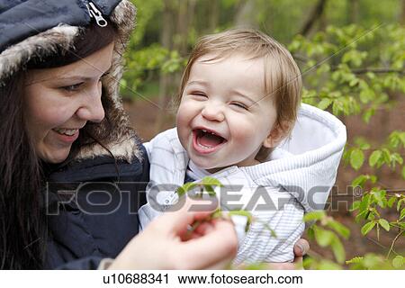 Stock Image - Smiling mother carrying son in forest. Fotosearch