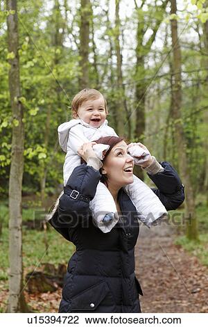 Stock Image - Smiling mother carrying son in forest. Fotosearch