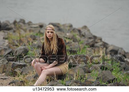 Stock Image - Teenage girl sitting on rocks. Fotosearch