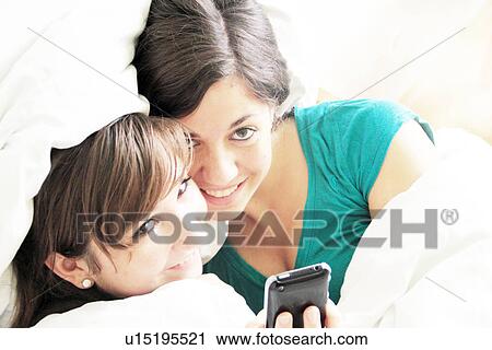 Teenage girls using cell phone in bed View Large Photo Image Stock Image - Teenage girls using cell phone in bed. Fotosearch