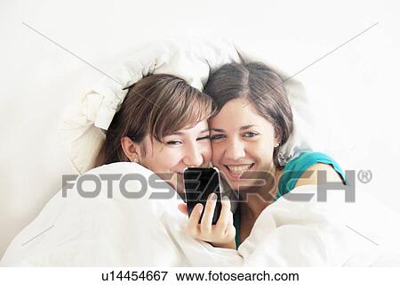 Stock Photo - Teenage girls using cell phone in bed. Fotosearch
