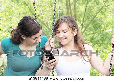 Stock Photo - Teenage girls using cell phone on swings. Fotosearch