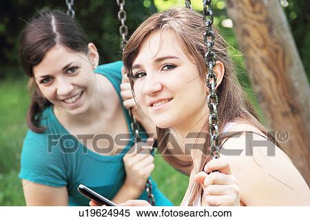 Teenage girls using cell phone on swings View Large Photo Image Stock Photography - Teenage girls using cell phone on swings. Fotosearch