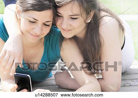 Stock Photo - Teenage girls using cell phone outdoors. Fotosearch