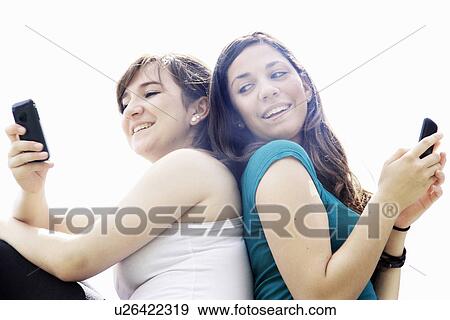 Stock Photo - Teenage girls using cell phones outdoors. Fotosearch