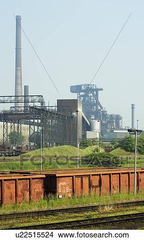Picture - Train running by steel factory. Fotosearch