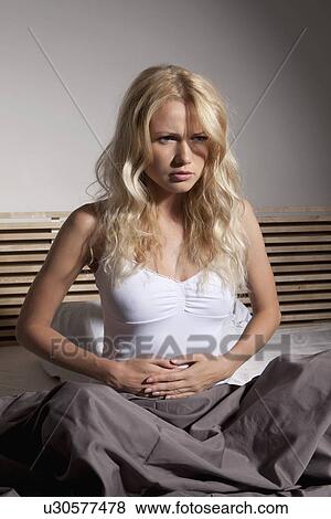 Stock Photo - Woman holding her belly in bed. Fotosearch