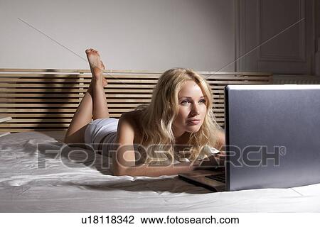 Stock Image - Woman using laptop on bed. Fotosearch