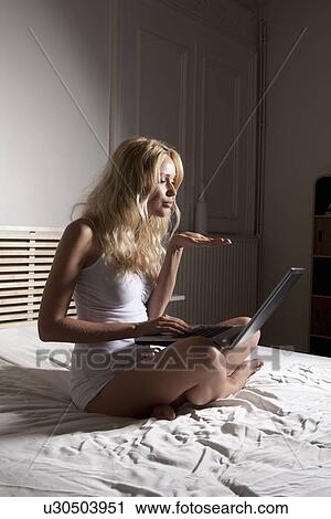 Stock Image - Woman using webcam on bed. Fotosearch