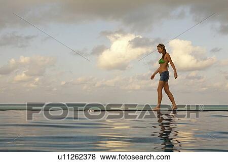 Stock Photo - Woman walking at edge of infinity pool. Fotosearch
