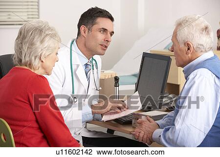 Stock Image - American doctor talking to senior couple in surgery. Fotosearch