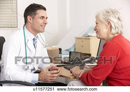 Stock Image - American doctor talking to senior woman in surgery. Fotosearch
