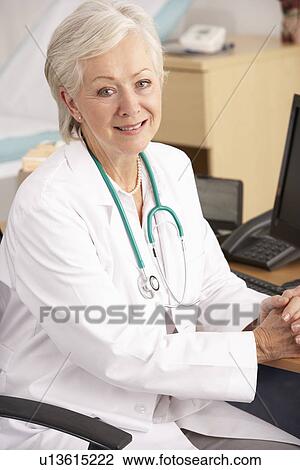 Stock Image - American female doctor sitting at desk. Fotosearch