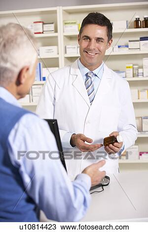 Stock Image - American pharmacist with senior man in pharmacy. Fotosearch