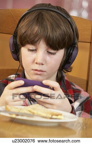 Boy Playing With Hand Held Games Console Whilst Eating Breakfast View Large Photo Image Stock Photograph - Boy Playing With Hand Held Games Console Whilst Eating Breakfast. Fotosearch