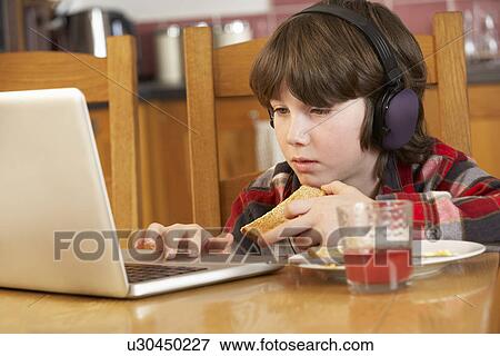 Stock Photo - Boy Using Laptop Whilst Eating Breakfast. Fotosearch