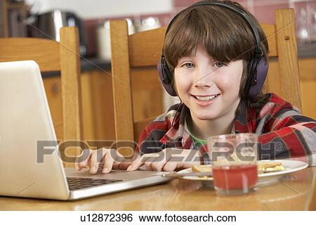 Stock Photograph - Boy Using Laptop Whilst Eating Breakfast. Fotosearch