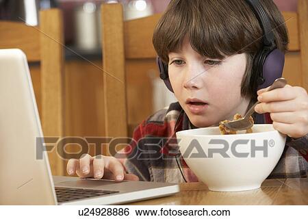 Stock Photograph - Boy Using Laptop Whilst Eating Breakfast. Fotosearch