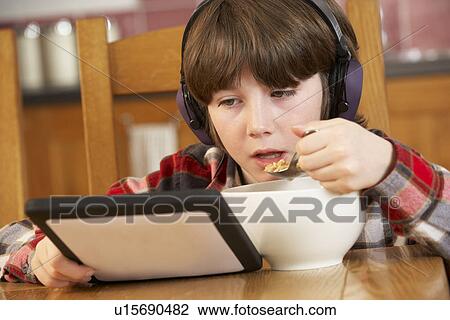 Stock Image - Boy Using Tablet Computer Whilst Eating Breakfast. Fotosearch