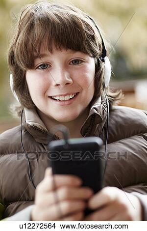 Picture - Boy Wearing Headphones And Listening To Music On Smartphone Wearing Winter Clothes. Fotosearch