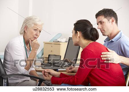 Stock Image - British GP talking to anxious couple in surgery. Fotosearch