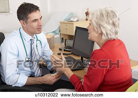 Stock Image - British GP talking to senior woman in surgery. Fotosearch