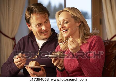 Stock Image - Couple Enjoying Slice Of Cake Sitting On Sofa. Fotosearch