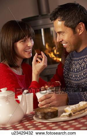 Stock Image - Couple Enjoying Tea And Cake By Cosy Log Fire. Fotosearch
